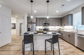 A modern kitchen with a center island, two chairs, and pendant lights.